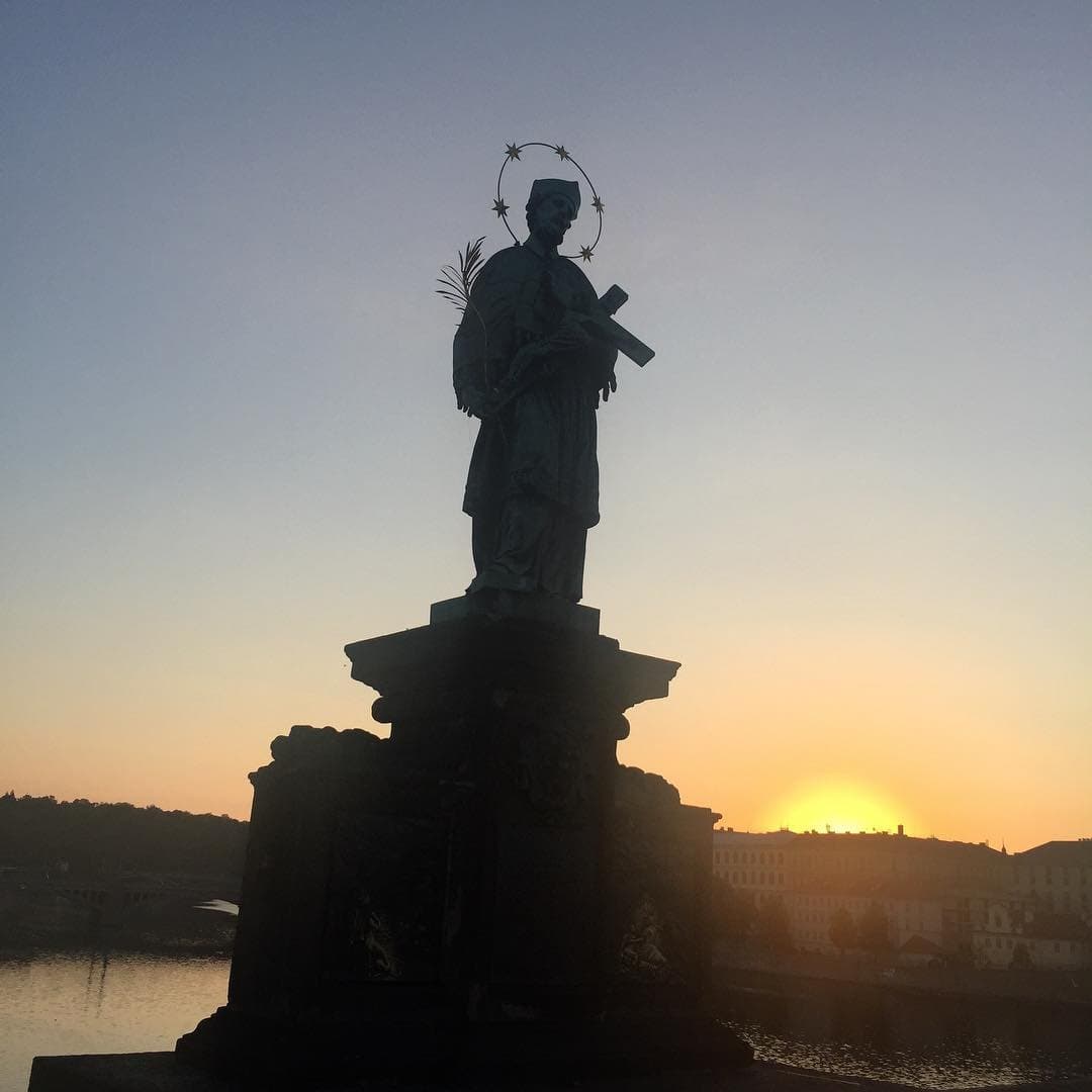 A statue silhouetted on Charles Bridge at sunrise